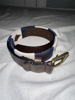 Mönstrat skärp från Pampeano - Lämna gärna in prisförslag)))Säljer ett snyggt bälte från Pampeano i brunt skinn med broderade mönster i marinblått och vitt. Bältet har en klassisk mässingsfärgad metallspänne och ett unikt geometriskt mönster längs hela remmen. Perfekt för att lyfta din outfit med lite extra stil.