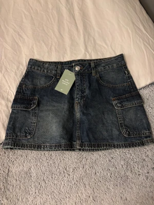 Mörkblå jeanskjol från H&M Divided - Säljer en mörkblå jeanskjol från H&M Divided i storlek 36. Kjolen har klassisk femficksdesign, stora sidofickor och knappstängning fram. Tillverkad av bomull med 20% återvunnen bomull. Aldrig använd!💗
