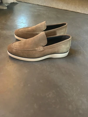 Beige mocka loafers från McGregor storlek 44 - Snygga loafers från McGregor i storlek 44. Skorna har en klassisk rund tå och stilren design som passar till många olika outfits. Perfekt för dig som gillar en clean och modern look.