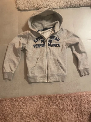 Zip up hoodie  - En grå zip up med text på framsidan. Från peak performance.  Lite slitna handleder💕