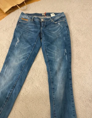 Blå jeans från ONLY med slits - Snygga blå jeans från ONLY med slitningar och rå kant längst ner på benen. Modellen har klassisk femficksdesign, normal passform och en slits på ena benet för en cool touch. Perfekt för dig som gillar en avslappnad och trendig stil.