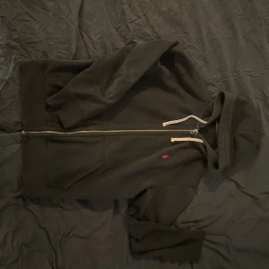 Svart hoodie från Polo Ralph Lauren - Svart hoodie från Polo Ralph Lauren med vit snörning och dragkedja framtill. Klassisk röd Polo-logga broderad på bröstet. Mjuk bomullskvalitet och huva för extra chill vibe. Perfekt för dig som gillar stilren streetwear. Storlek L men Passar även M!