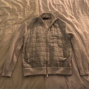 Grå stickad cardigan jacka Michel Axel - Snygg grå cardigan jacka från Michel Axel Paris i storlek 50. Jackan har quiltad framsida, ribbstickade ärmar och rygg, samt två fickor med dragkedja. Perfekt för dig som gillar stilren och modern look med bekväm passform. Priset är diskuterbart vid snabb affär. Nypris ca 4000 kr 