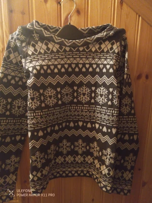 Svart och vit stickad tröja med snöflingor från Rusta - Mysig stickad tröja i svart och vitt med vinterinspirerat mönster av snöflingor, hjärtan och geometriska former. Tröjan har långärmad design och passar perfekt för kalla dagar. Materialet är mjukt och värmande, och mönstret ger en riktigt vintrig vibe.