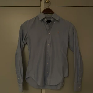 Ralph Lauren Skjorta - Riktigt fet skjorta från Ralph Lauren! Klassisk krage och knappar hela vägen. Ikoniska broderade loggan på bröstet. Skjortan har lång ärm med manschett och är tillverkad i mjuk bomull. Jag är 170 lång och väger 57 kg, den passar perfekt på mig! Perfekt för dig som gillar stilrena och tidlösa plagg.