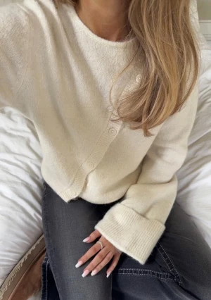Krämvit kofta med breda ärmslut från Gina Tricot - Supermysig krämvit kofta från Gina Tricot med breda ribbstickade ärmslut och rund hals. Koftan har en unik sned knäppning med små knappar framtill och är tillverkad i mjuk stickad ullmix. Perfekt för lager-på-lager och chill dagar.