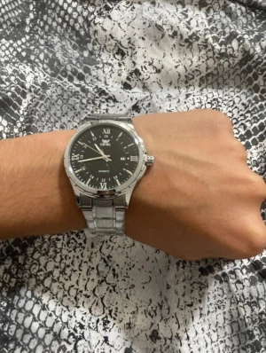 OPK silverfärgad herrklocka - KAN DISKUTERA PRISET PRIVAT                                                                          Stilren herrklocka från OPK med svart urtavla och romerska siffror. Klockan har ett klassiskt runt boett i silverfärgat metall och matchande länkarmband. Quartz-urverk och datumvisning. Perfekt för dig som gillar en clean och modern look.