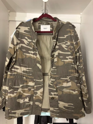 Camouflage jacka från ONLY - Säljer en grön och beige camouflage jacka från ONLY i storlek L. Jackan har flera stora fickor framtill, knappar och klassisk krage. Är i storlek L men skulle mer säga att det är som en M