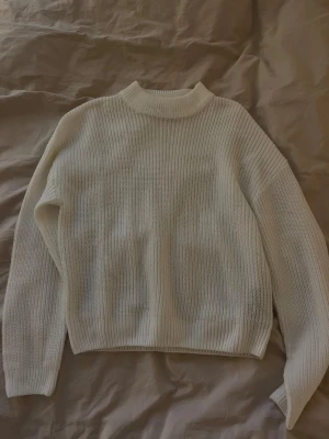 Vit stickad tröja med hög krage - Säljer en vit stickad tröja med ribbad struktur och hög krage. Tröjan har långärmade och en loose passform som ger en chill och avslappnad vibe. Perfekt att slänga på sig när det är lite kyligt ute.