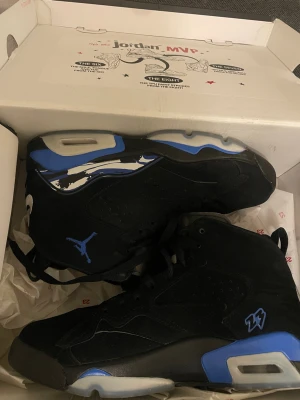 Jordan MVP sneakers svart/blå - Jordan MVP sneakers i svart och blått med coola detaljer som Jumpman-logga och siffran 23 på sidan. Skorna har högt skaft, snörning och en platt sula med blå och grå inslag. Materialet är mocka och syntet, och designen har en sportig vibe med unika mönster på sulan.