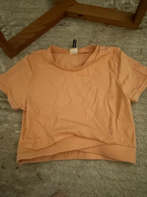 Persikofärgad croppad topp PrettyLittleThing - Säljer en persikofärgad croppad topp från PrettyLittleThing i storlek 36. Toppen har rund halsringning och korta ärmar, tillverkad i mjuk bomull. Perfekt för dig som gillar enkel och fräsch stil med en touch av färg. Tränings material, perfekt till gymmet😻