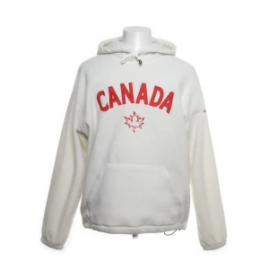 Vit fleece hoodie från New Era Canada - Säljer en vit hoodie från New Era Canada med röd CANADA-text och lönnblad på bröstet. Tröjan är i mjuk fleece, har huva med snörning och en stor magficka. Perfekt för kyliga dagar och har en loose passform.
