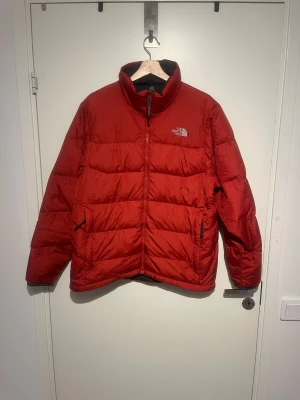  The North Face dunjacka - Säljer en röd The North Face-dunjacka i storlek L, i bra skick. Jackan har dragkedja framtill, två sidofickor med dragkedja och justerbara muddar med knapp. Perfekt för kalla dagar med sin varma och puffiga design.  Pris kan diskuteras. Skicks gärna, bud. 