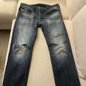 Blå jeans från Diesel - Snygga blå jeans från Diesel med slitna detaljer och en cool tvätt. De har en tapered passform och är perfekta för en avslappnad stil. W33 L32, gör gärna av dig vid minsta lila fundering