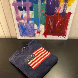 Mörkblå stickad tröja med amerikansk flagga - Mörkblå stickad tröja med en stor amerikansk flagga framtill. Tröjan har rund halsringning och långa ärmar. Perfekt för dig som gillar klassisk och preppy stil.