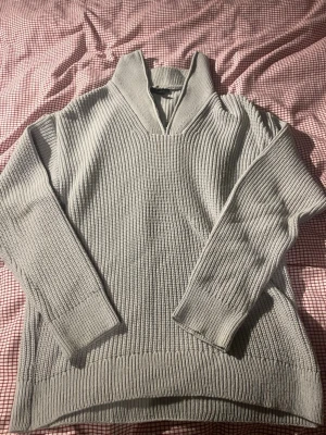 Ljusgrå ribbad stickad tröja - Säljer en ljusgrå stickad tröja med ribbad struktur och v-ringad krage. Tröjan har långärmade och breda muddar vid ärmslut och nederkant. Perfekt för lager-på-lager och chill stil. Materialet är mjukt och grovstickat, vilket ger en skön och avslappnad känsla. En perfekt quarter Zip                OBS: liten fläck som är med på bilden men syns knappast 