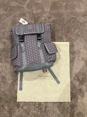 Grå ryggsäck med mönster - Snygg grå ryggsäck med ikoniskt geometriskt mönster och detaljer i skinn. Väskan har två sidofickor med lock, justerbara axelremmar och spännen framtill. Perfekt för dig som vill ha en lyxig och unik väska med cool design.