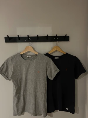 Grå och svart t-shirt Les Deux - Två stilrena t-shirts från Les Deux i storlek 158/164. Ena är grå och den andra mörkblå. Diskret broderad II-logga i orange på bröstet. Sköna i mjuk bomull, perfekta för en chill look.