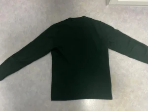 Mörkgrön stickad tröja från Levi's - Snygg mörkgrön stickad tröja från Levi's med rund hals och diskret röd logotyp på bröstet. Tröjan har ribbade muddar vid ärmslut och nederkant, samt långärmad passform. Perfekt för dig som gillar klassisk stil med en twist. Pris kan diskuteras