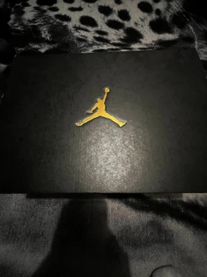 Jordan Max Aura 4 Black/Gold sneakers - Säljer ett par Jordan Max Aura 4 sneakers i svart, metallic guld och vitt. Skorna har en hög siluett med snörning, guldiga detaljer och vit sula med synlig dämpning. Perfekta för dig som vill sticka ut med en sportig och modern look.