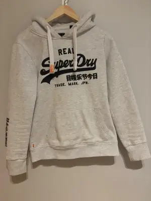 En stilren Superdry hoodie i färgen grå med svart tryck. Den är knapp använd och är i superbra skick! Det står storlek M i den men sitter mer som storlek S. Pris kan diskuteras! 