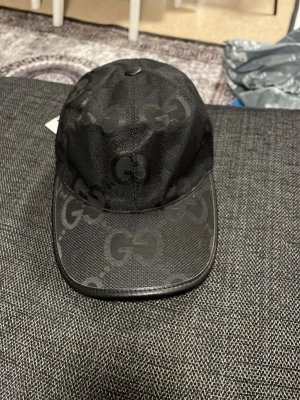 Svart kaps keps med mönster - Snygg svart keps från Fendi med det klassiska -mönstret över hela kepsen. Justerbar rem baktill med metallspänne och -tag. Materialet är slitstark polyester med en lätt glansig finish. Perfekt för dig som vill ha en lyxig streetwear-accessoar.