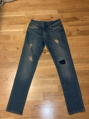 Slim fit jeans från Pier One Denim - Slim fit blå jeans från Pier One Denim DPT Berlin med slitna detaljer och hål på benen. Klassisk femficksmodell med knapp och dragkedja. Snyggt tvättad denim som ger en cool look, perfekt för dig som gillar streetstyle.