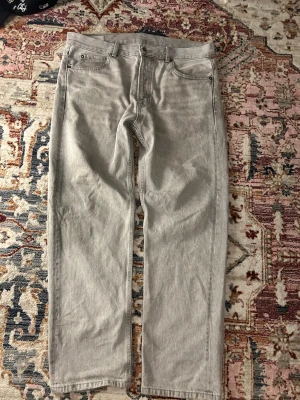Grå raka jeans från Zara, strl 44 - Snygga grå jeans från Zara i rak modell med klassiska fem fickor och bälteshällor. Jeansen har en neutral grå ton och är tillverkade i jeansmaterial. Passar dig som gillar enkel och clean stil.
