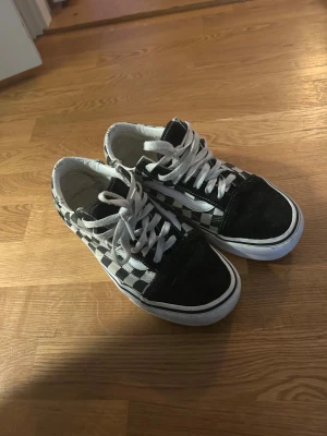 Svarta och vita Vans Old Skool sneakers - Säljer ett par Vans Old Skool sneakers med klassiskt svart och vitt rutigt mönster på sidorna, vit sula och snörning. Skorna har rund tå och är tillverkade i mocka och canvas. Perfekt för dig som gillar streetstyle och skate-vibe.