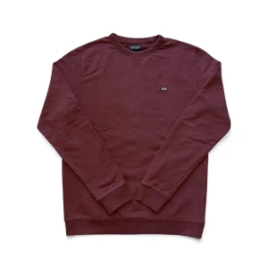 Mörkröd sweatshirt från Lexington - Snygg mörkröd sweatshirt från Lexington i storlek M. Tröjan har rund hals, ribbade muddar och ett litet Lexington-flag patch på bröstet. Perfekt för dig som gillar klassisk och clean stil. Använd en del men inga märkbara defekter