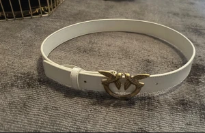 Vitt skärp/bälte från Pinko med fågelspänne - Snyggt vitt skärp från Pinko med ett ikoniskt guldfärgat spänne med två fåglar. Skärpet är tillverkat i slätt skinn och har stilrena sömmar längs kanterna. Perfekt accessoar för att lyfta din outfit med en cool detalj!! 85 cm🤍🤍🤍🤍