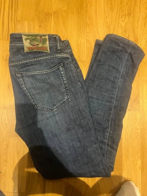 Mörkblå jeans från Jacob Cohen, stl 34 - Säljer ett par snygga mörkblå jeans från Jacob Cohen i klassisk femficksmodell. Jeansen har diskreta kontrastsömmar, exklusiv patch bak och är tillverkade i mjukt denimtyg. Perfekt passform och italiensk design för dig som gillar stilrena jeans.