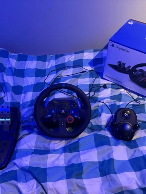 Logitech G29 ratt,pedaler och växelspak PS4/PS5/PC - Säljer en Logitech G29 Driving Force ratt med pedaler och växelspak för PlayStation. Ratten är svart med blå och röda detaljer, tillverkad i läder och plast. Perfekt för racing- och bilspel, med realistisk force feedback och robust konstruktion.