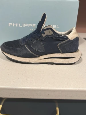 Blå sneakers från Philippe Model - Snygga sneakers från Philippe Model i mörkblå mocka och textil med beige detaljer. Skorna har klassisk snörning och en vit, som ger en cool kontrast. Perfekta för dig som gillar stilrena men ändå sportiga sneakers. NYPRIS 3000 TVÄTT INGÅR!