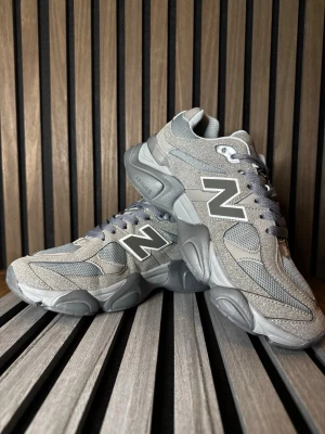 Grå New Balance sneakers i mocka - Snygga grå sneakers från New Balance med chunky sula och klassisk N-logga på sidan. Skorna har en mix av mocka och meshpaneler för både stil och andningsförmåga. De har snörning och en sportig vibe som passar perfekt till streetwear.