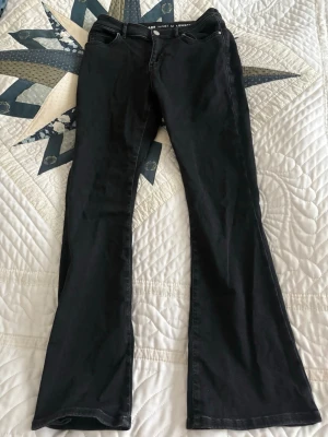 Svarta bootcut jeans med hög midja - Snygga svarta bootcut jeans med hög midja och klassisk femficksdesign. Jeansen har en tidlös look och är tillverkade i ett mjukt jeansmaterial som sitter bekvämt. Perfekta för dig som gillar en retroinspirerad siluett.