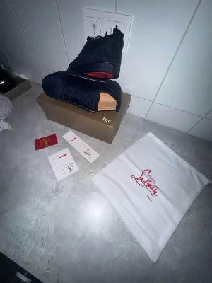 Mörkblåa sneakers från Louboutin - Snygga mörkblåa sneakers från Christian Louboutin i mocka med klassisk röd sula. Skorna har rund tå, snörning och diskret branding. Kommer med originalpåse och tillbehör. Perfekta för dig som vill ha något exklusivt och stilrent.