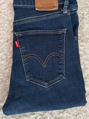 Levi's Mile High Super Skinny Jeans blå W28L30 - Snygga mörkblå Levi's Mile High Super Skinny jeans med klassisk femficksdesign och hög midja. Jeansen har den ikoniska röda Levi's-lappen på bakfickan och är tillverkade i stretchig denim för en tight passform.