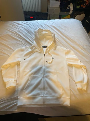 Vit zip hoodie från Polo Ralph Lauren - Snygg vit hoodie med dragkedja från Polo Ralph Lauren. Klassisk design med huva och dragsnören, två stora fickor framtill och den ikoniska broderade loggan på bröstet. Tillverkad i mjukt bomullsmaterial som känns skönt mot huden. Perfekt för en clean och stilren look.