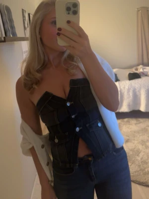 Mörkblå denim korsett med knappar - Trendig mörkblå korsettopp i denim med markerade sömmar och stora silvriga knappar framtill. Toppen är croppad och axelbandslös, perfekt för en edgy look. Snygg att styla med jeans eller kjol. 🩵🩵🩵