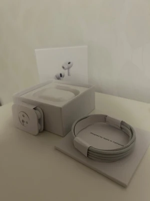 Apple AirPods Pro 2 - Säljer ett par vita Apple AirPods Pro 2 med trådlöst laddningsetui. Hörlurarna har en stilren och kompakt design i blank plast och levereras med originalförpackning och USB-C laddkabel. Perfekta för dig som vill ha grymt ljud och smidig anslutning till din iPhone.