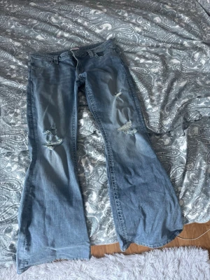 Blå bootcut jeans  - Säljer ett par ljusblå bootcut jeans med slitna detaljer på båda benen. Köpta på Gina Tricot, men använda en gång 
