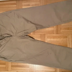 Beige chinos med rak passform, herr storlek 38/30 - Snygga beige chinos med klassisk rak passform och diskreta fickor både fram och bak. Tillverkade i mjuk bomull som känns skön mot huden. Perfekta för en clean och avslappnad stil. Saknas en knapp på ena bakfickan. 