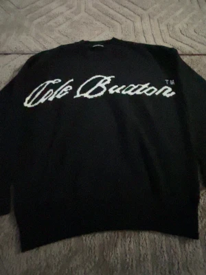 Svart stickad tröja Cole Buxton - Säljer en svart stickad tröja från Cole Buxton med vit broderad logga över bröstet. Tröjan har rund halsringning, långa ärmar och ribbade muddar vid ärmslut och nederkant. Perfekt för dig som gillar streetwear och enkel stil.