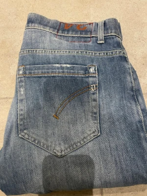 Blå jeans från dondup - Säljer ett par blå jeans från dondup femficksmodell och snygga slitningar. Jeansen har en slim passform och är tillverkade i mjukt denimtyg med dondup logan på bakfickan. Perfekta för en avslappnad och stilren look. Jeans passar någon som bär 34 33 32 i midjan