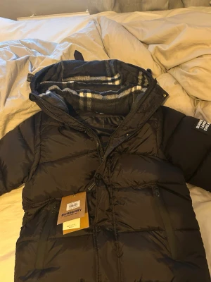 Svart dunjacka från Burberry med huva - Snygg svart från Burberry. Jackan har två sidofickor med dragkedja. Den är i perfekt skick, den var för liten för mig.