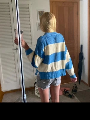Blåvit randig stickad tröja - Säljer en oversized stickad tröja med breda blå och vita ränder. Tröjan har rund halsringning, långa ärmar och ribbade muddar. Perfekt för en chill och avslappnad stil. Materialet är mjukt och skönt, troligtvis bomullsblandning.