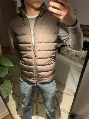Brun dunväst från Bondelid med dragkedja - Snygg brun dunväst från Bondelid med ståkrage och två fickor med dragkedja framtill. Nypris 1100❌ mitt pris 950 ✅Västen har quiltad design och stängs med en tvåvägsdragkedja. Perfekt att slänga över en hoodie eller tröja för extra värme. Enkel och stilren look som passar till det mesta.