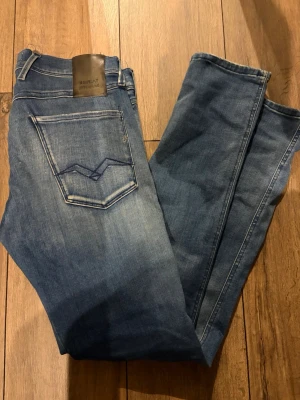 Blå Replay Hyperflex jeans - Snygga blå Replay Hyperflex jeans med klassisk femficksdesign och skinnpatch bak i midjan. Jeansen har en lätt tvättad look och raka ben. Perfekta för dig som vill ha både stil och komfort i vardagen.