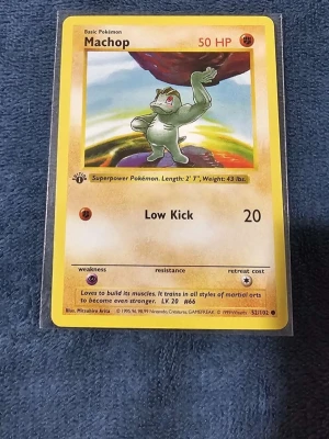 Machop #52 1st Edition  - Machop Pokémonkort från Base Set, nummer 52/102. Kortet har gul ram och motiv av Machop mot en färgglad bakgrund. Text och detaljer på engelska. Perfekt för samlare eller Pokémonfans som vill utöka sin kortsamling.
